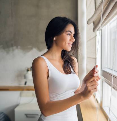 young attractive woman looking in window in the morning in bedroom young attractive woman looking in window in the morning in bedroom